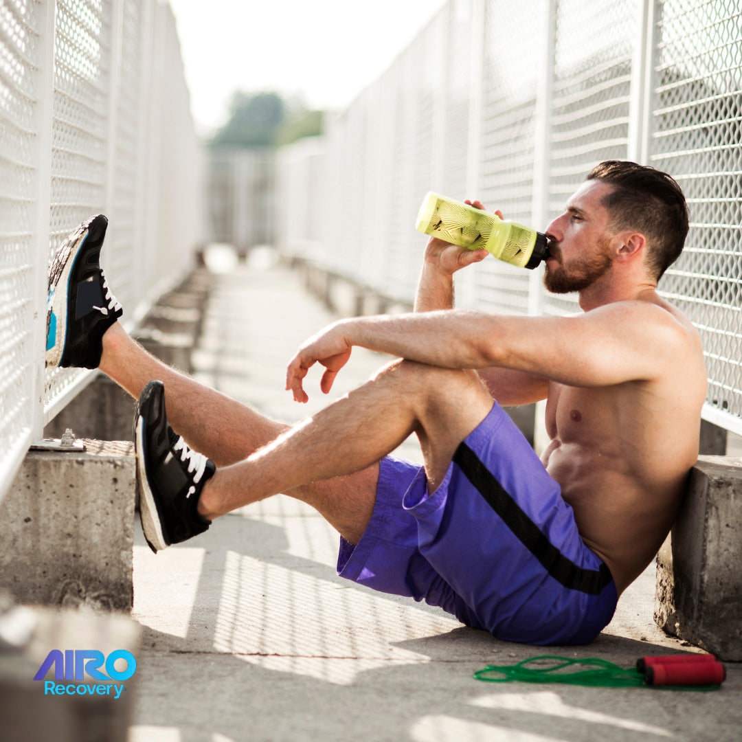 Shirtless athlete resting by a fence, drinking water with a jump rope nearby; AIRO Recovery logo included.